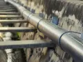 Metalowa rura biegnie wzdłuż betonowego koryta. To element kanalizacji ciśnieniowej, transportującej wodę.