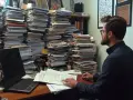 Pracownik z okularami tonie w papierach, próbując zdążyć ze sprawozdaniem BDO po terminie.