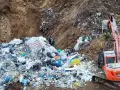 Ogromna góra śmieci, tworząca nielegalne wysypisko, z koparką w tle. Widać worki, folie i różne odpady.