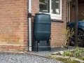 Zbiornik na wodę opadową przy ceglanym domu, zbierający deszczówkę z rynny. Ekologiczne rozwiązanie dla ogrodu.