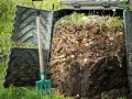 Kompostownik pełen resztek organicznych, obok zielone widły. Proces kompostowania w ogrodzie, numer 200201.