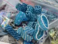 Zbliżenie na ręcznie robione pierścionki i bransoletki z niebieskich koralików w plastikowych woreczkach.