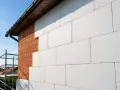 Ściana domu w trakcie ocieplania. Widoczne cegły i biały styropian nro. W tle rusztowanie i niebo.