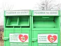 Dwa zielone kontenery na odzież używaną, z napisem "POJEMNIK NA ODZIEŻ UŻYWANĄ" i sercem z symbolami recyklingu.