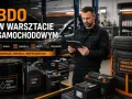 Mechanik w warsztacie samochodowym korzysta z tabletu, zarządzając odpadami i ewidencją. Obok stoją beczki z zużytymi olejami i akumulatory.