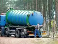 Pracownik podłącza wąż do beczkowozu w celu wywozu osadu z oczyszczalni przydomowej. Przepisy dotyczące takich działań są kluczowe.