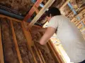 Pracownik montuje wełnę mineralną w konstrukcji dachu. Utylizacja wełny mineralnej to ważny etap budowy.