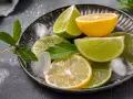 Plasterki cytryny i limonki, kostki lodu i listki mięty na metalowej tacy. Orzeźwiający zapach cytrusów, w tym limonen, unosi się w powietrzu.