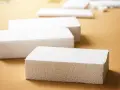 Białe bloki styropianu na brązowym tle. Czy styropian wygłusza? Ten materiał może być odpowiedzią na Twoje pytania o izolację akustyczną.
