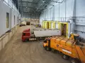 Wielka hala przemysłowa, gdzie trwa termiczne przekształcanie odpadów. Ciężarówki z odpadami czekają na rozładunek, a koparka przygotowuje materiał do przetworzenia.