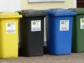 Cztery kolorowe kosze na śmieci: żółty na folię, czarny na metale, niebieski na papier i zielony na szkło. Różne rodzaje koszy ułatwiają segregację.