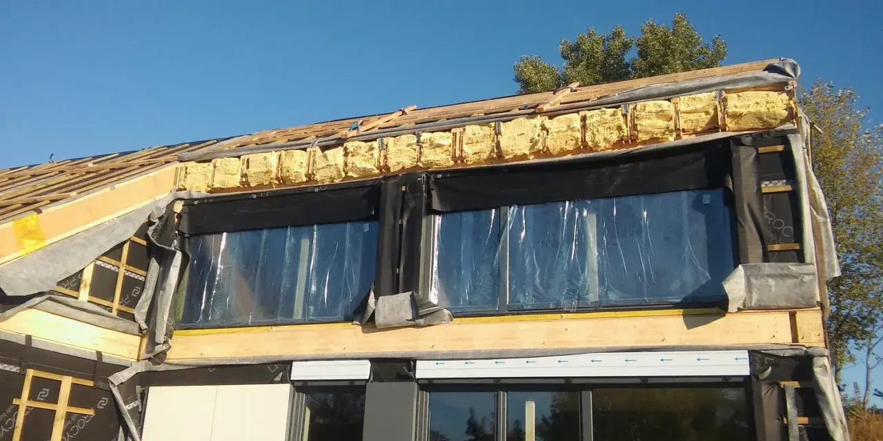 Budowa domu w toku: widoczne drewniane elementy konstrukcji, pianka montażowa i folia świadczą o postępach w pracach nad termoizolacją budynku.