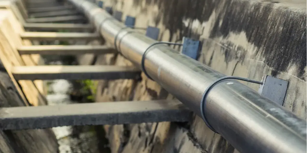 Metalowa rura biegnie wzdłuż betonowego koryta. To element kanalizacji ciśnieniowej, transportującej wodę.