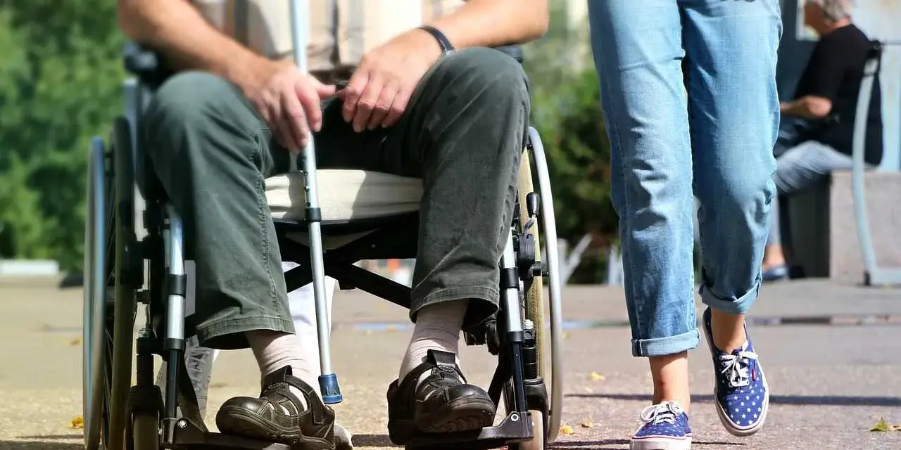 Osoba na wózku inwalidzkim z laską obok idącej osoby. Ulga na śmieci dla niepełnosprawnych to ważny temat.