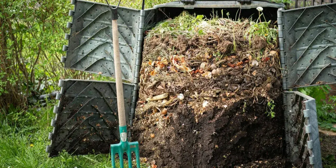 Kompostownik pełen resztek organicznych, obok zielone widły. Proces kompostowania w ogrodzie, numer 200201.