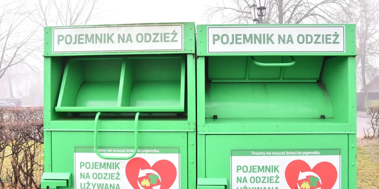 Dwa zielone kontenery na odzież używaną, z napisem "POJEMNIK NA ODZIEŻ UŻYWANĄ" i sercem z symbolami recyklingu.