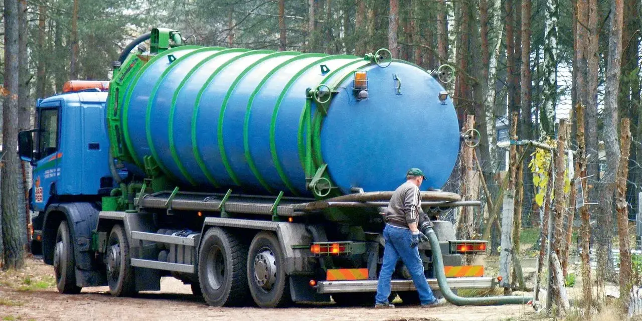 Pracownik podłącza wąż do beczkowozu w celu wywozu osadu z oczyszczalni przydomowej. Przepisy dotyczące takich działań są kluczowe.
