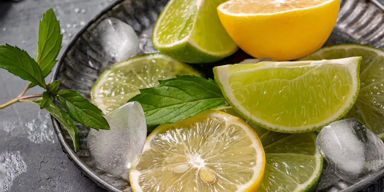 Plasterki cytryny i limonki, kostki lodu i listki mięty na metalowej tacy. Orzeźwiający zapach cytrusów, w tym limonen, unosi się w powietrzu.