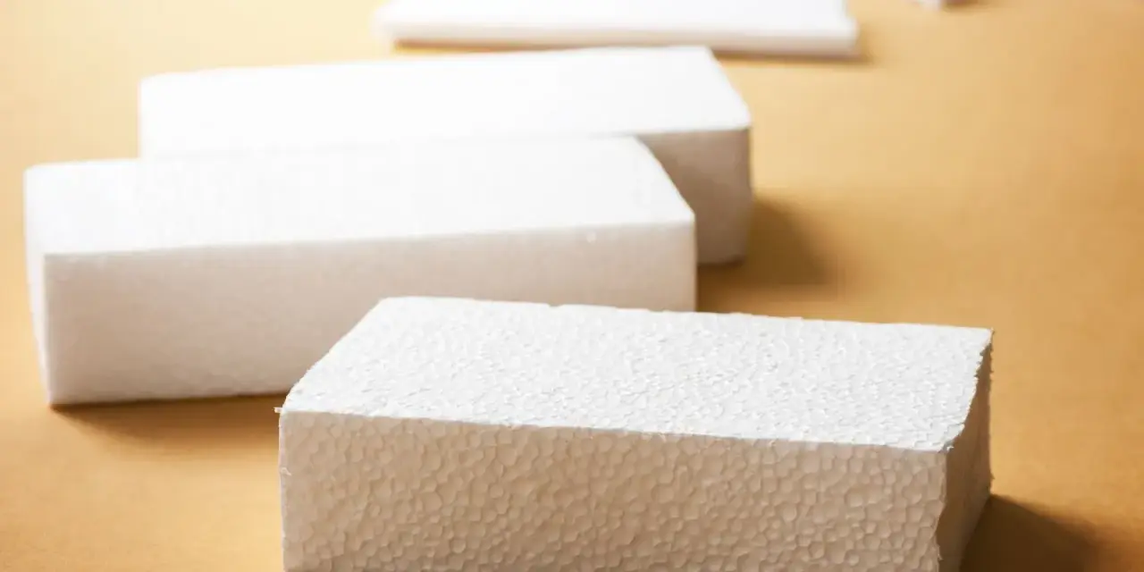 Białe bloki styropianu na brązowym tle. Czy styropian wygłusza? Ten materiał może być odpowiedzią na Twoje pytania o izolację akustyczną.