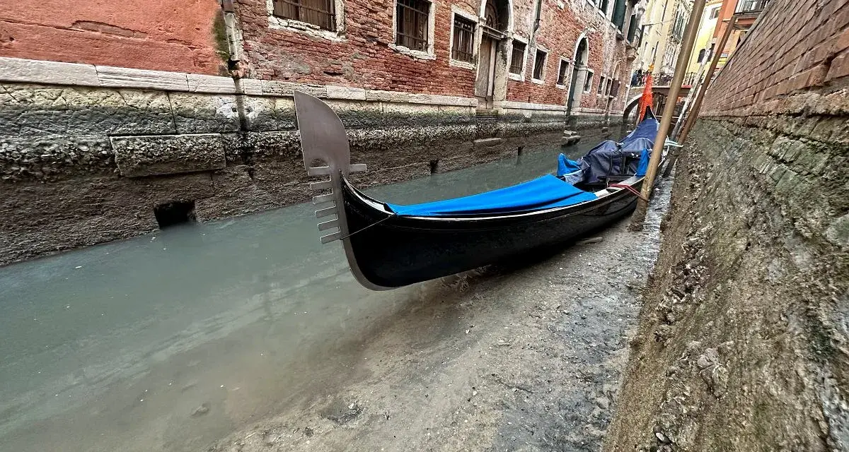 Wąski kanał w Wenecji, gdzie widać, jak są odprowadzane ścieki. Przy brzegu zacumowana gondola.