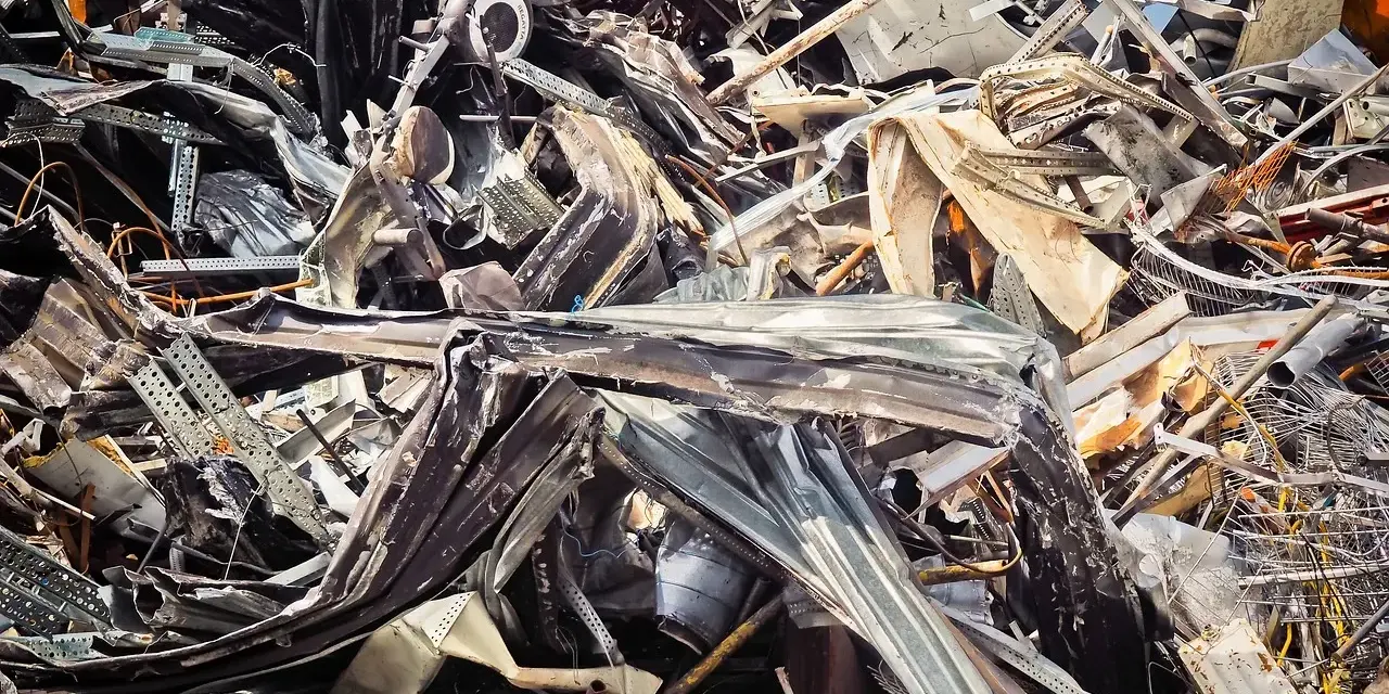 Góra złomu, poskręcane metalowe elementy, tworzące chaotyczną strukturę. Widoczne fragmenty blachy, prętów i innych odpadów. Kod odpadu: 17 04 05.