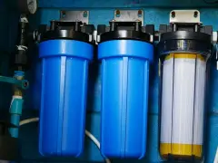 System filtrów do wody, który oczyszcza wodę. Dwa niebieskie filtry i jeden przezroczysty z białym wkładem.