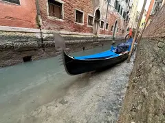 Wąski kanał w Wenecji, gdzie widać, jak są odprowadzane ścieki. Przy brzegu zacumowana gondola.