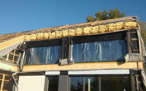 Budowa domu w toku: widoczne drewniane elementy konstrukcji, pianka montażowa i folia świadczą o postępach w pracach nad termoizolacją budynku.
