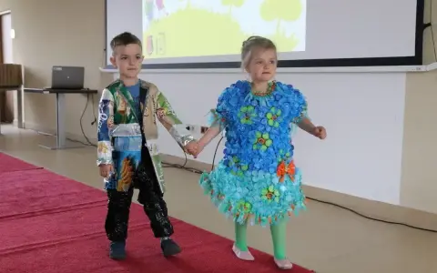 Chłopiec prezentuje strój z recyklingu, wykonany z opakowań po przekąskach. Jego koleżanka ma sukienkę z nakrętek.