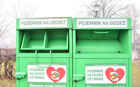 Dwa zielone kontenery na odzież używaną, z napisem "POJEMNIK NA ODZIEŻ UŻYWANĄ" i sercem z symbolami recyklingu.