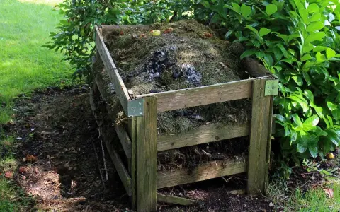 Drewniany kompostownik wypełniony trawą, liśćmi i resztkami organicznymi. To idealne miejsce na odpady zielone, kod odpadu 20 02 01.