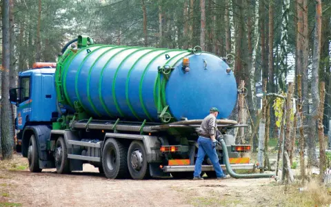 Pracownik podłącza wąż do beczkowozu w celu wywozu osadu z oczyszczalni przydomowej. Przepisy dotyczące takich działań są kluczowe.