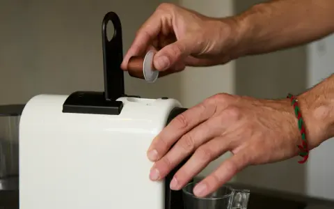 Ręka wkłada kapsułkę do ekspresu. Zastanawiasz się, gdzie wyrzucać kapsułki po kawie? To pierwszy krok do pysznej kawy.