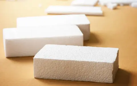 Białe bloki styropianu na brązowym tle. Czy styropian wygłusza? Ten materiał może być odpowiedzią na Twoje pytania o izolację akustyczną.
