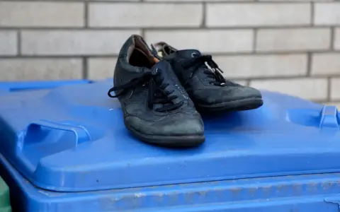 Stare, czarne buty leżą na niebieskim koszu na śmieci. Czas zastanowić się, gdzie wyrzucić stare buty, by dać im drugie życie.