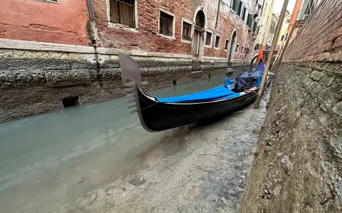 Wąski kanał w Wenecji, gdzie widać, jak są odprowadzane ścieki. Przy brzegu zacumowana gondola.