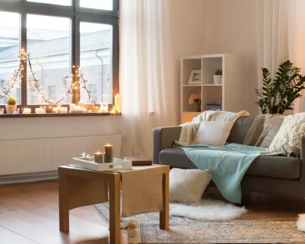 Jak ocieplić zimny pokój? Przytulne wnętrze z kanapą, kocami, świecami i lampkami tworzy ciepłą atmosferę.