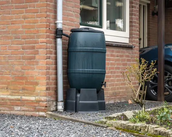 Zbiornik na wodę opadową przy ceglanym domu, zbierający deszczówkę z rynny. Ekologiczne rozwiązanie dla ogrodu.