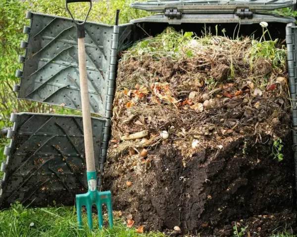 Kompostownik pełen resztek organicznych, obok zielone widły. Proces kompostowania w ogrodzie, numer 200201.