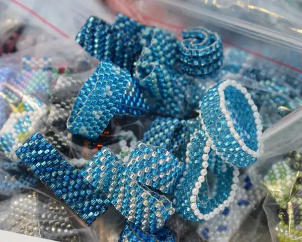 Zbliżenie na ręcznie robione pierścionki i bransoletki z niebieskich koralików w plastikowych woreczkach.