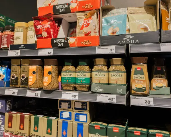 Półka sklepowa z kawą mieloną i rozpuszczalną. Gdzie wyrzucić opakowanie po kawie mielonej? Zazwyczaj do plastiku lub papieru, zależnie od materiału.