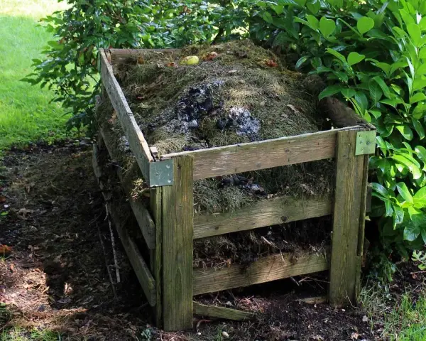 Drewniany kompostownik wypełniony trawą, liśćmi i resztkami organicznymi. To idealne miejsce na odpady zielone, kod odpadu 20 02 01.