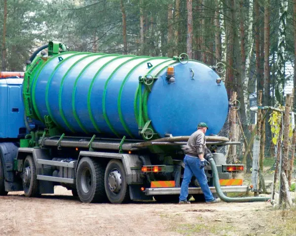 Pracownik podłącza wąż do beczkowozu w celu wywozu osadu z oczyszczalni przydomowej. Przepisy dotyczące takich działań są kluczowe.