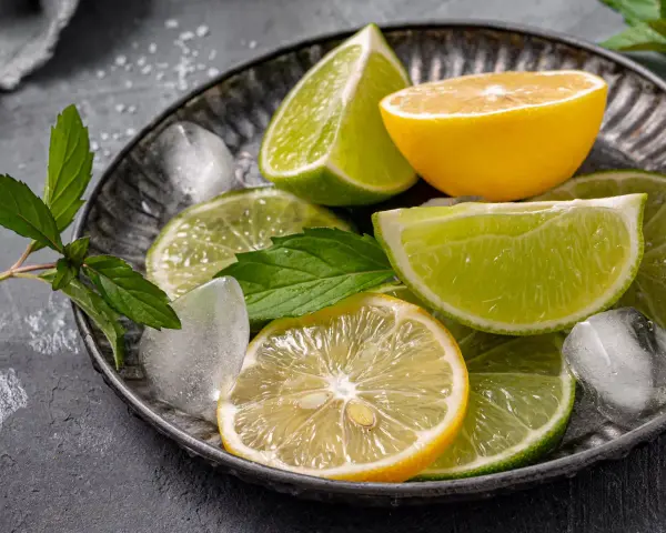 Plasterki cytryny i limonki, kostki lodu i listki mięty na metalowej tacy. Orzeźwiający zapach cytrusów, w tym limonen, unosi się w powietrzu.