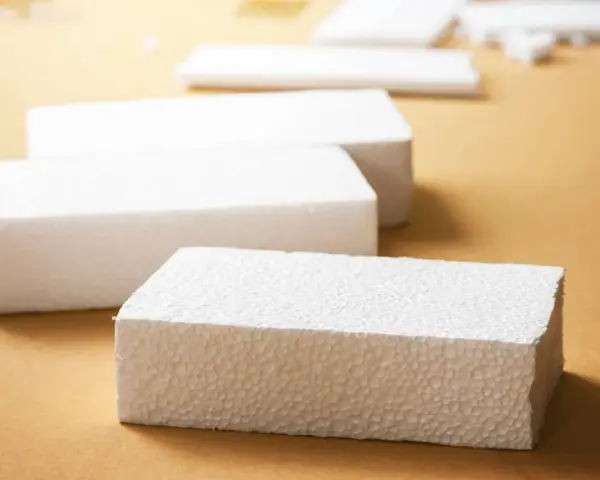 Białe bloki styropianu na brązowym tle. Czy styropian wygłusza? Ten materiał może być odpowiedzią na Twoje pytania o izolację akustyczną.