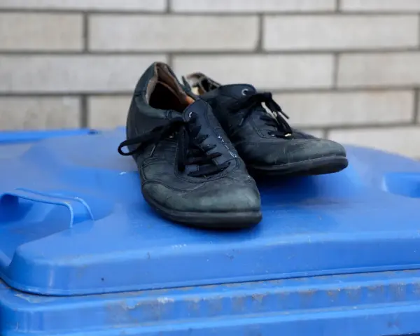 Stare, czarne buty leżą na niebieskim koszu na śmieci. Czas zastanowić się, gdzie wyrzucić stare buty, by dać im drugie życie.