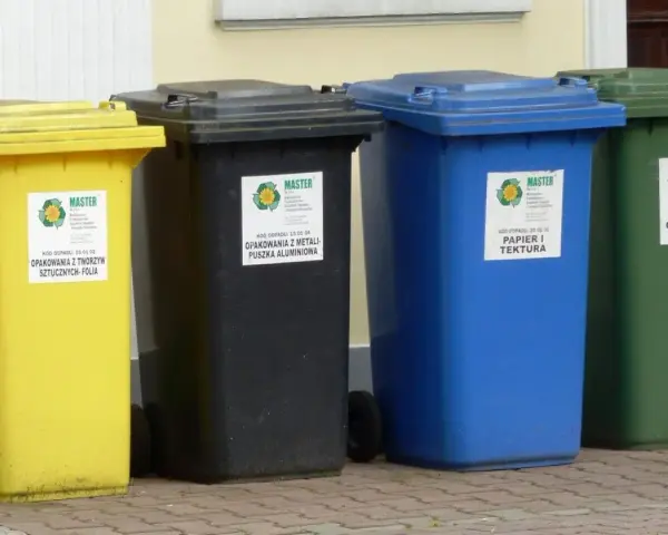 Cztery kolorowe kosze na śmieci: żółty na folię, czarny na metale, niebieski na papier i zielony na szkło. Różne rodzaje koszy ułatwiają segregację.