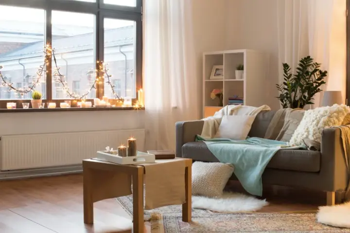 Jak ocieplić zimny pokój? Przytulne wnętrze z kanapą, kocami, świecami i lampkami tworzy ciepłą atmosferę.