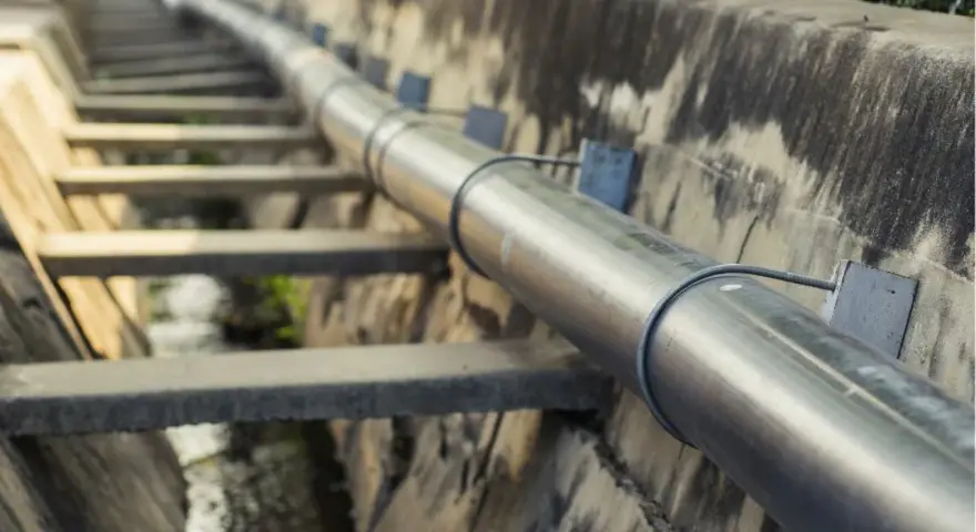 Metalowa rura biegnie wzdłuż betonowego koryta. To element kanalizacji ciśnieniowej, transportującej wodę.