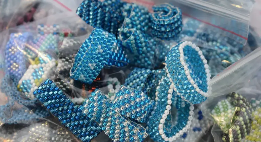 Zbliżenie na ręcznie robione pierścionki i bransoletki z niebieskich koralików w plastikowych woreczkach.